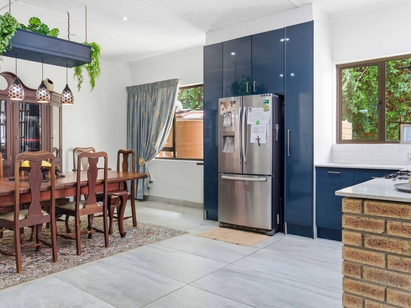 Open-plan kitchen and dining area featuring modern blue cabinetry, stone countertops, a brick-based island, and large format floor tiles.