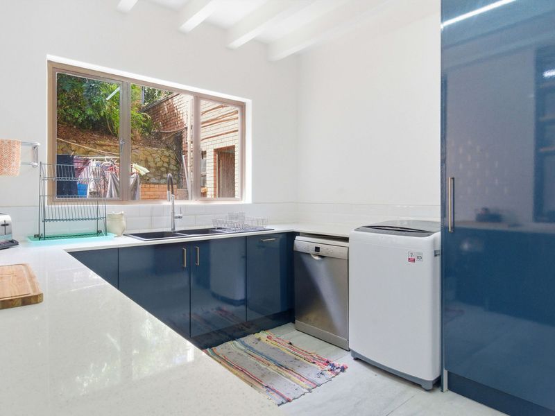 A modern scullery featuring sleek blue cabinetry, white quartz countertops, subway tile backsplash, and exposed ceiling beams, providing a functional and stylish prep area.