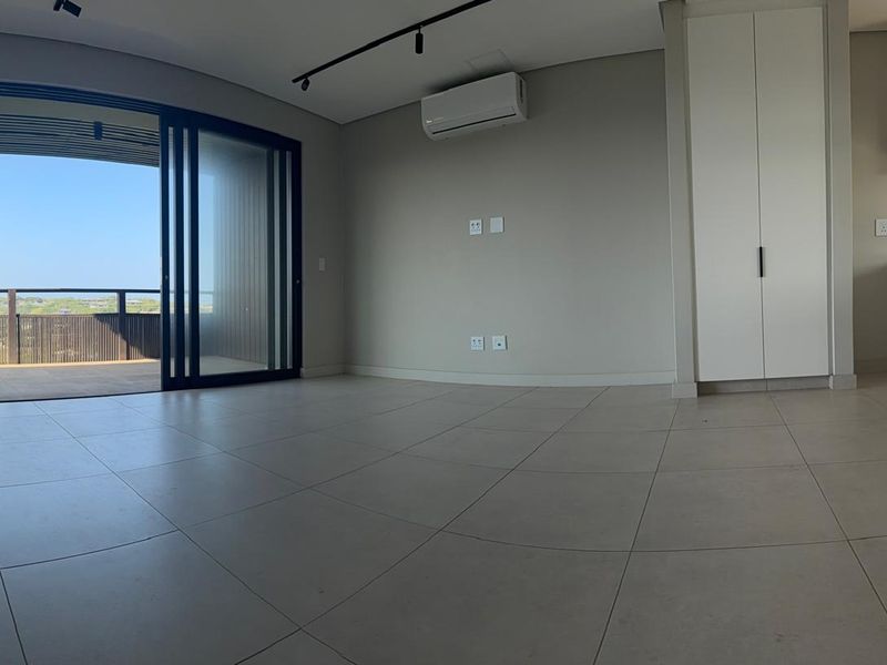 Modern open-plan living area featuring large format floor tiles, built-in storage, split-system air conditioning, and seamless access to a private balcony.