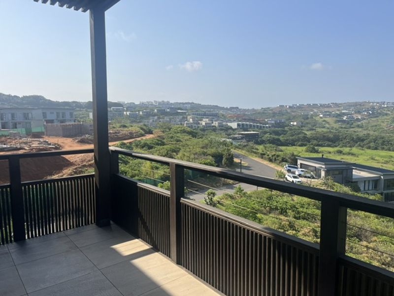 A modern covered balcony featuring tiled flooring and a stylish slatted timber balustrade, offering expansive views over the surrounding estate and landscape.