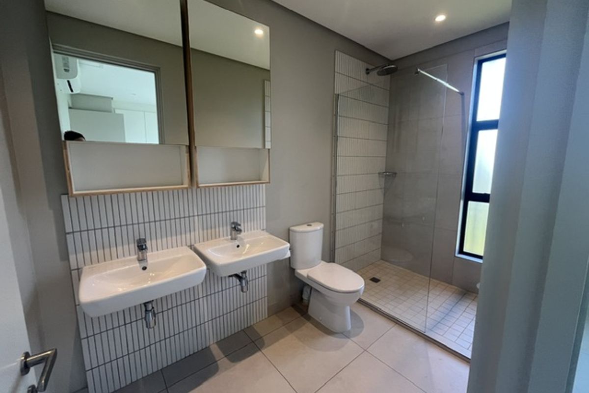 Modern bathroom featuring a double vanity with wall-mounted basins, mirrored cabinets, and a spacious walk-in shower with a glass screen.