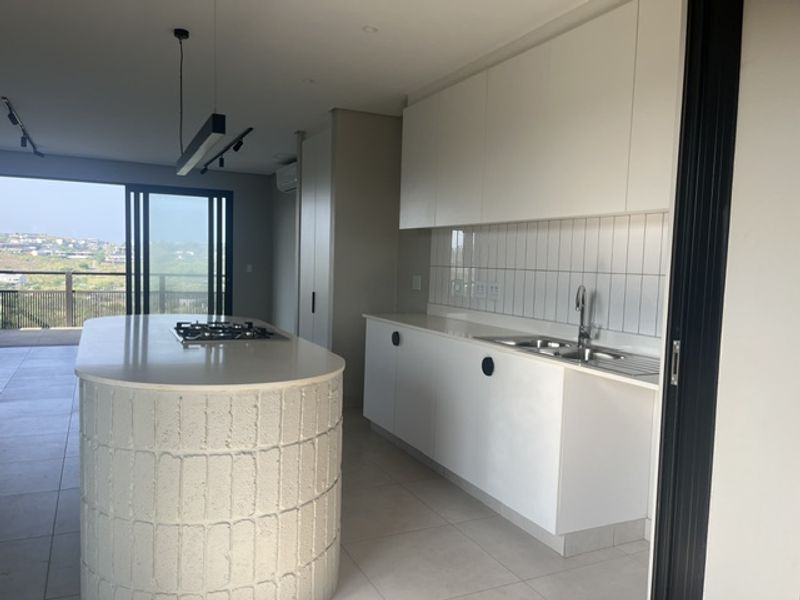 Modern open-plan kitchen featuring a textured island with a built-in gas hob, sleek white cabinetry, and direct access to a balcony with scenic views.