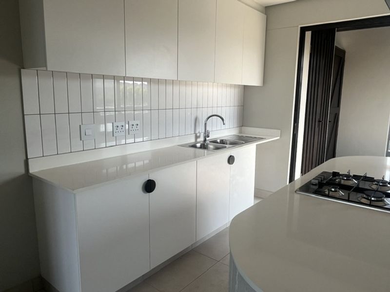 Modern kitchen featuring sleek white cabinetry, quartz countertops, a subway tile backsplash, and a central island with an integrated gas hob.