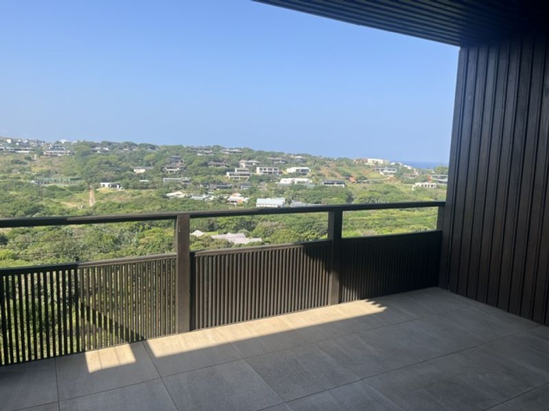 A modern covered balcony featuring high-quality timber cladding, a sleek slat balustrade, and large format floor tiles with expansive coastal views.