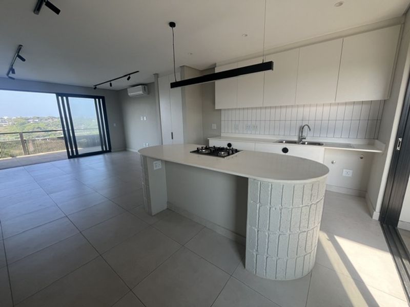 Modern open-plan living area featuring a sleek kitchen with a curved island, gas hob, and seamless access to a balcony with scenic views.