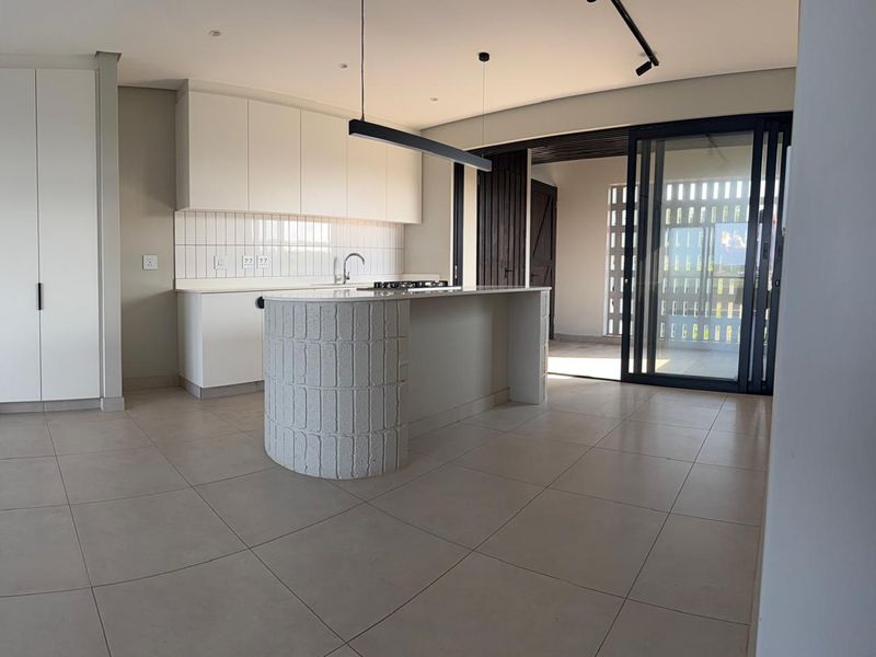 Modern open-plan kitchen featuring a curved island, sleek white cabinetry, subway tile backsplash, and seamless access to an outdoor patio area.