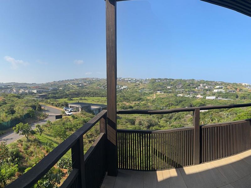 Spacious covered balcony featuring a timber slatted balustrade and expansive elevated views over the surrounding landscape and coastal estate.