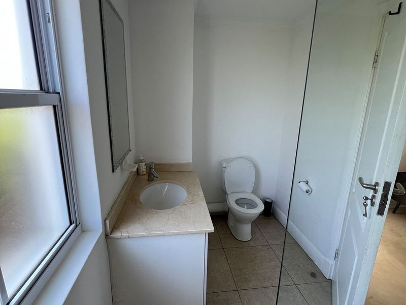 A functional bathroom featuring a vanity with stone countertop, integrated sink, toilet, and a glass shower screen.