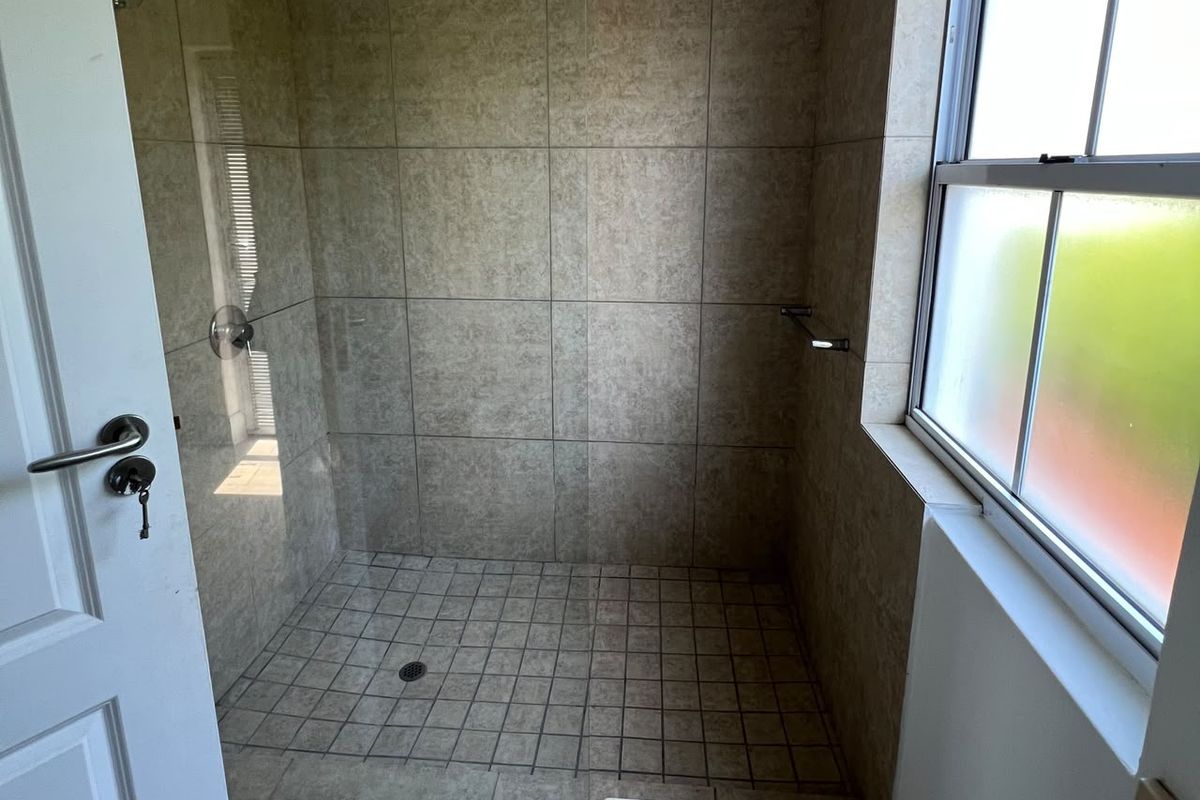 A clean walk-in shower featuring neutral wall tiles, a tiled floor, and a frosted window for natural light and privacy.