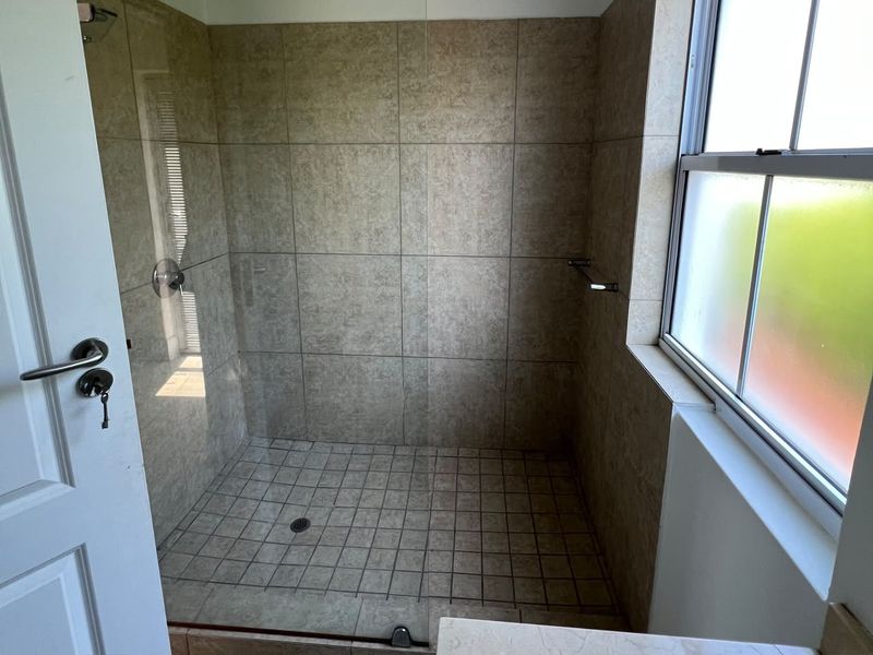 A clean walk-in shower featuring neutral wall tiles, a tiled floor, and a frosted window for natural light and privacy.