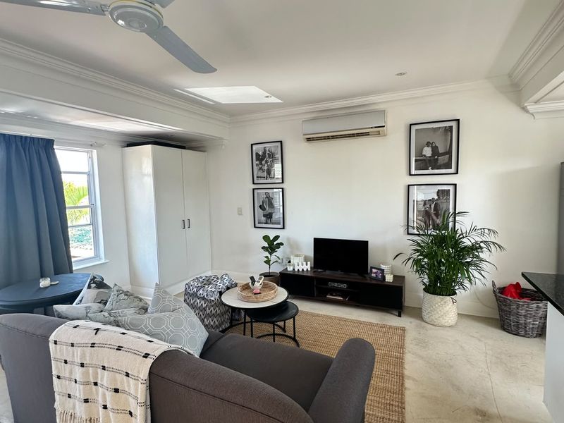A bright living room featuring tiled flooring, a ceiling fan, a skylight, and a wall-mounted split-system air conditioner.