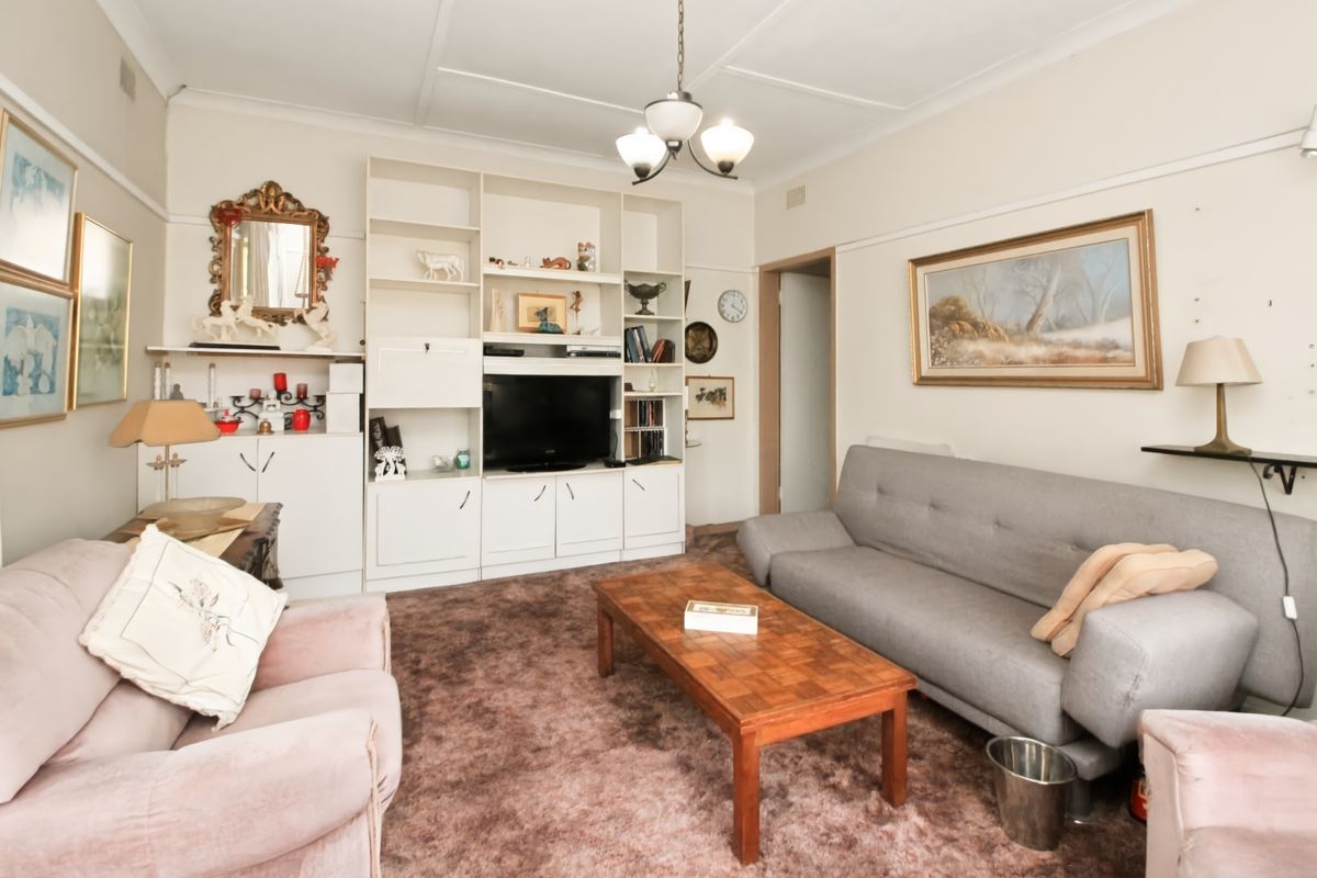 A living room featuring a large built-in shelving unit and traditional ceiling cornice, currently finished with dated carpet flooring.