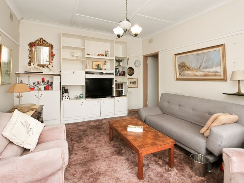 A living room featuring a large built-in shelving unit and traditional ceiling cornice, currently finished with dated carpet flooring.