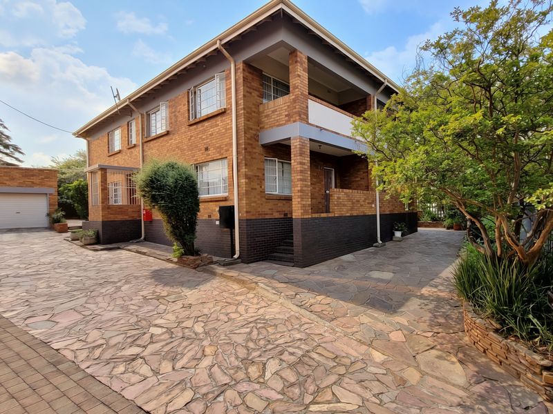 A well-maintained face brick apartment building featuring a paved driveway, integrated garage, and balcony access.