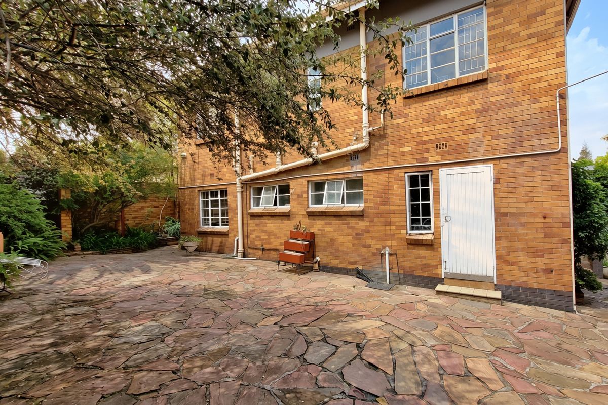 Rear exterior view of the apartment building featuring a stone-paved patio area and traditional brick facade with established garden surroundings.