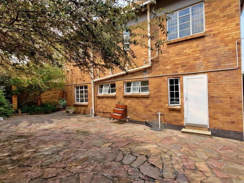 Rear exterior view of the apartment building featuring a stone-paved patio area and traditional brick facade with established garden surroundings.