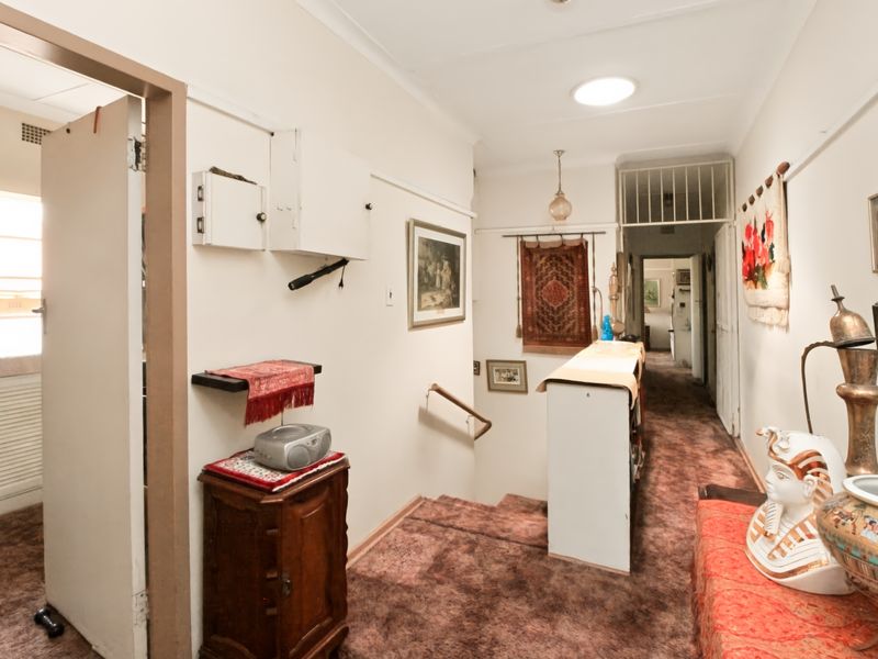 A functional hallway featuring a staircase with a handrail, overhead lighting, and a skylight, providing access to adjacent rooms within the apartment.