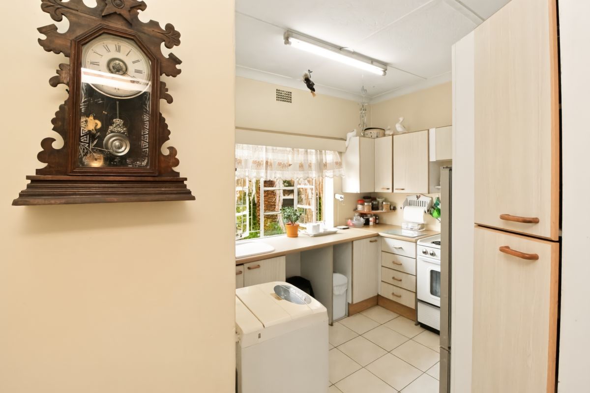 A functional kitchen featuring dated cabinetry, laminate countertops, a freestanding stove, and tiled flooring, offering potential for a modern renovation.