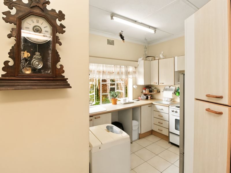 A functional kitchen featuring dated cabinetry, laminate countertops, a freestanding stove, and tiled flooring, offering potential for a modern renovation.