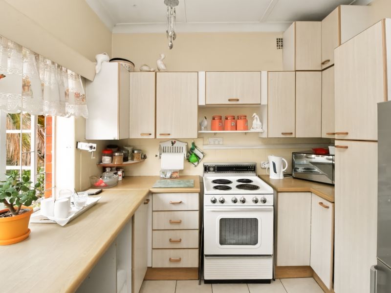 A functional kitchen featuring light wood-tone cabinetry, laminate countertops, and a freestanding electric stove, with natural light provided by a side window.