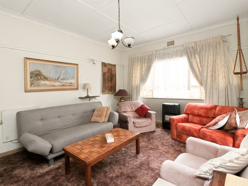 A living room featuring a classic picture rail, ceiling light fixture, and large window with curtain tracks, currently finished with dated carpeting.