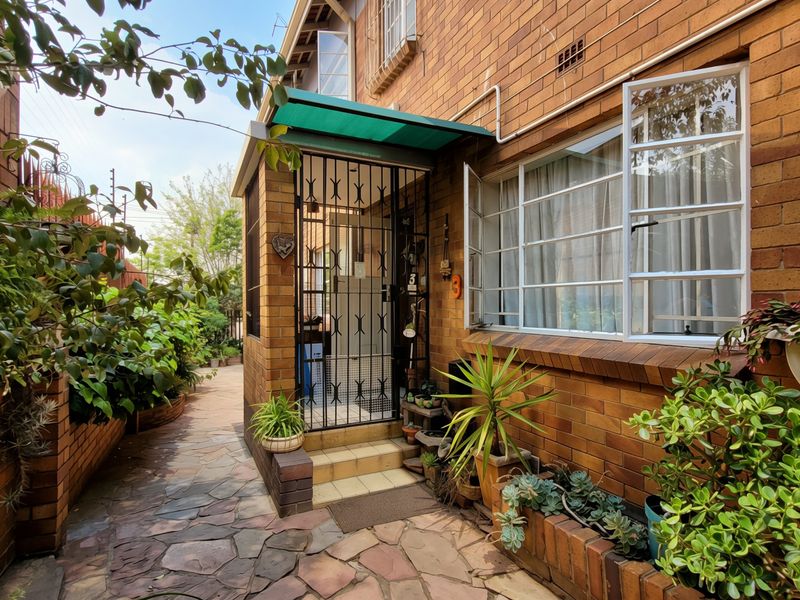 Front entrance of a face brick apartment unit featuring a security gate, paved walkway, and established garden planter boxes.