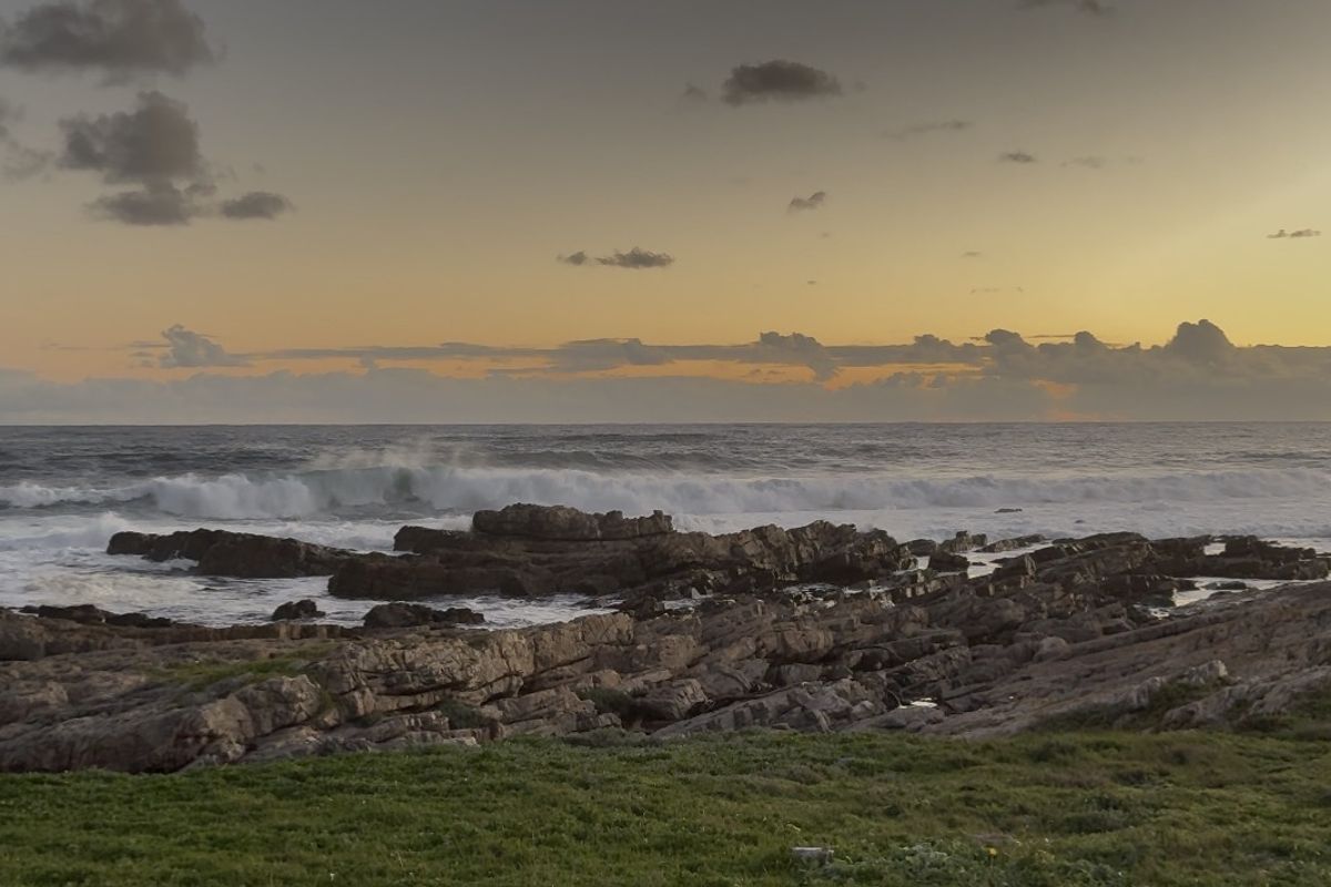 A scenic coastal view featuring rocky shoreline and ocean waves at sunset.