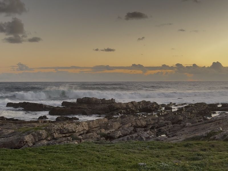 A scenic coastal view featuring rocky shoreline and ocean waves at sunset.