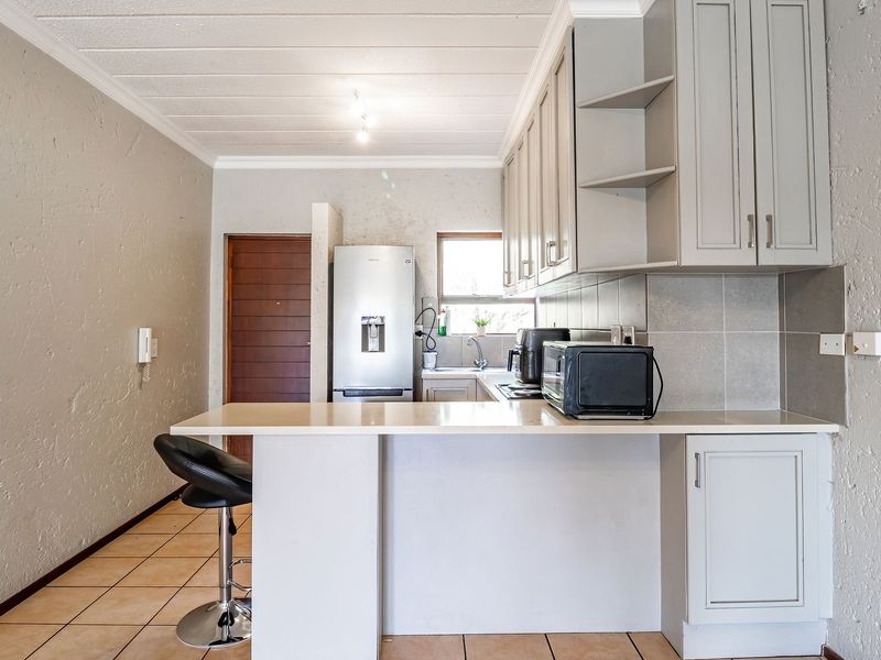 A functional kitchen featuring light-toned built-in cabinetry, a breakfast bar, tiled backsplash, and tiled flooring, offering a practical layout for daily use.