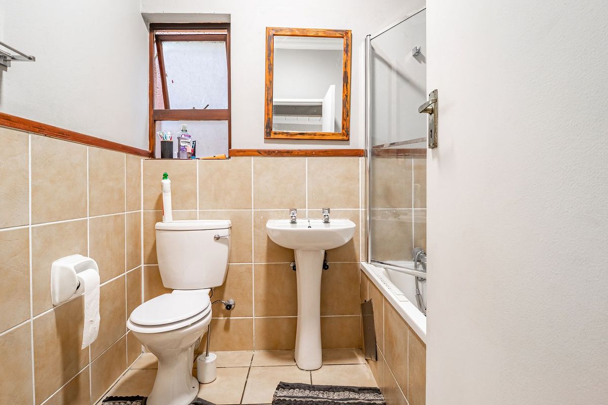 A functional bathroom featuring a pedestal basin, toilet, and a shower-over-bath combination with a glass screen, finished with neutral wall and floor tiling.