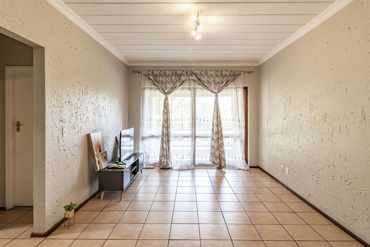 A spacious living room featuring tiled flooring, textured walls, and a sliding glass door that provides access to the outdoor area.