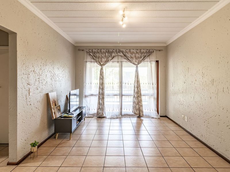 A spacious living room featuring tiled flooring, textured walls, and a sliding glass door that provides access to the outdoor area.