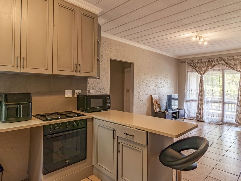 Open-plan kitchen and living area featuring tiled floors, built-in cabinetry with integrated oven and hob, and direct access to an outdoor patio.