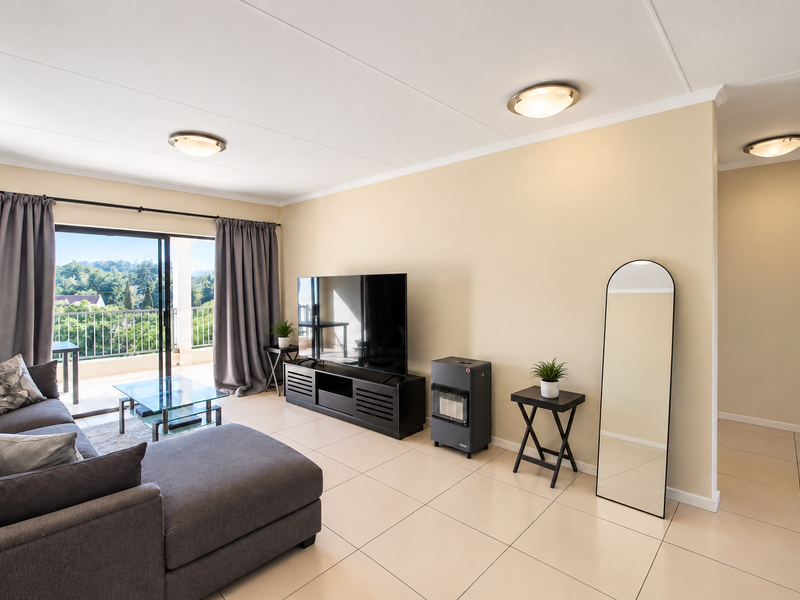 Spacious living room featuring neutral tiled flooring, ceiling lighting, and direct access to a private balcony through large sliding glass doors.