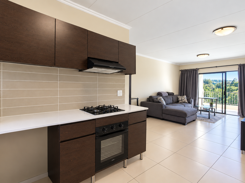 Modern open-plan kitchen and living area featuring dark wood cabinetry, built-in appliances, tiled floors, and direct access to a balcony with scenic views.