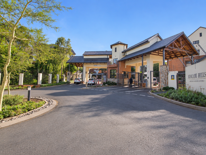 The main entrance and security gatehouse of Kyalami Hills estate, featuring a paved driveway, landscaped gardens, and secure access control.