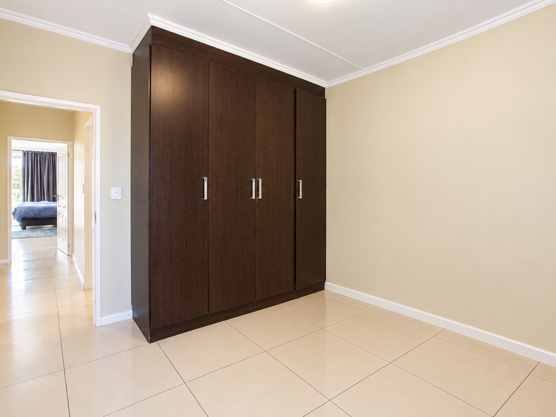A clean, empty bedroom featuring neutral walls, tiled flooring, crown molding, and a large dark wood built-in wardrobe.