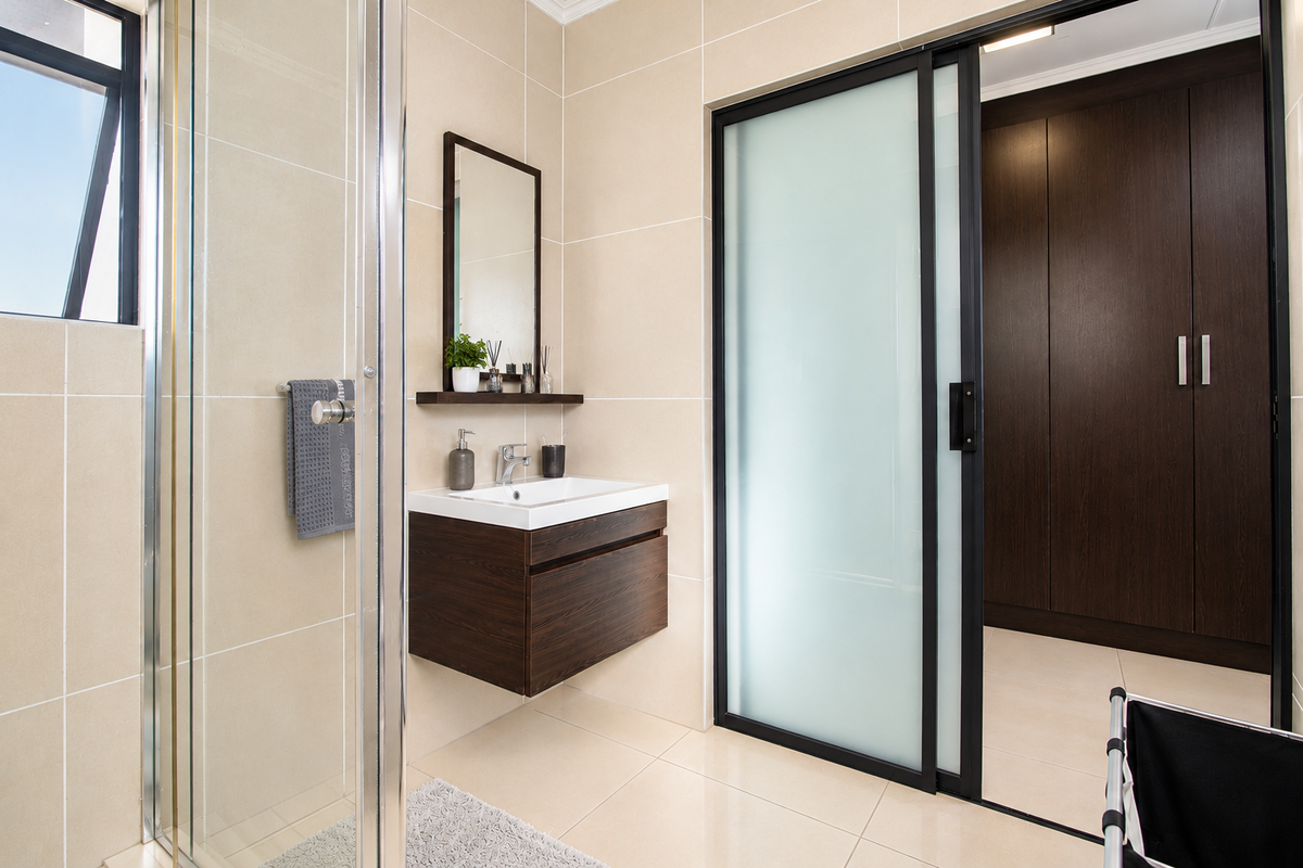 Modern bathroom featuring a floating vanity, glass shower enclosure, and a sliding door leading to a dressing area with built-in cupboards.