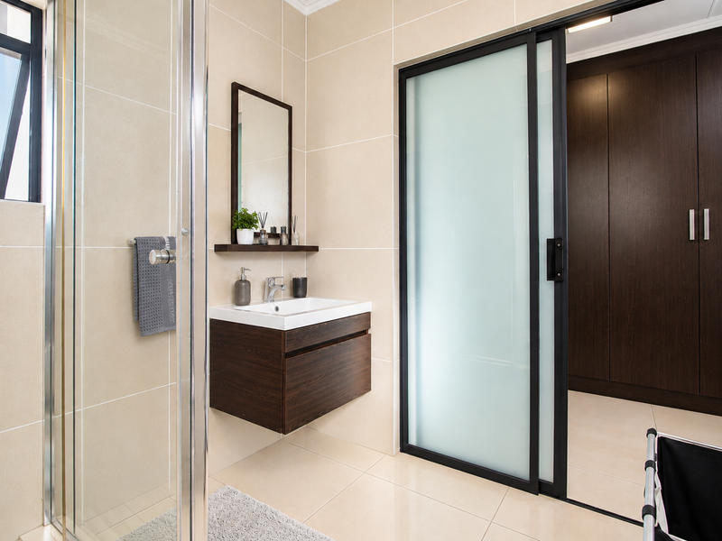 Modern bathroom featuring a floating vanity, glass shower enclosure, and a sliding door leading to a dressing area with built-in cupboards.