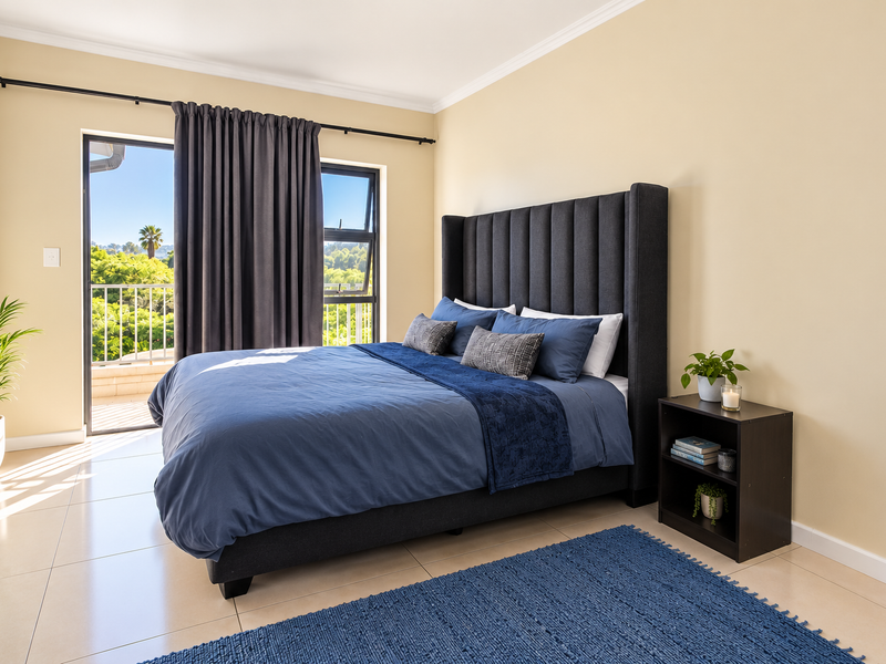 A bright and well-maintained bedroom featuring tiled flooring, a large sliding glass door leading to a balcony, and neutral wall finishes.