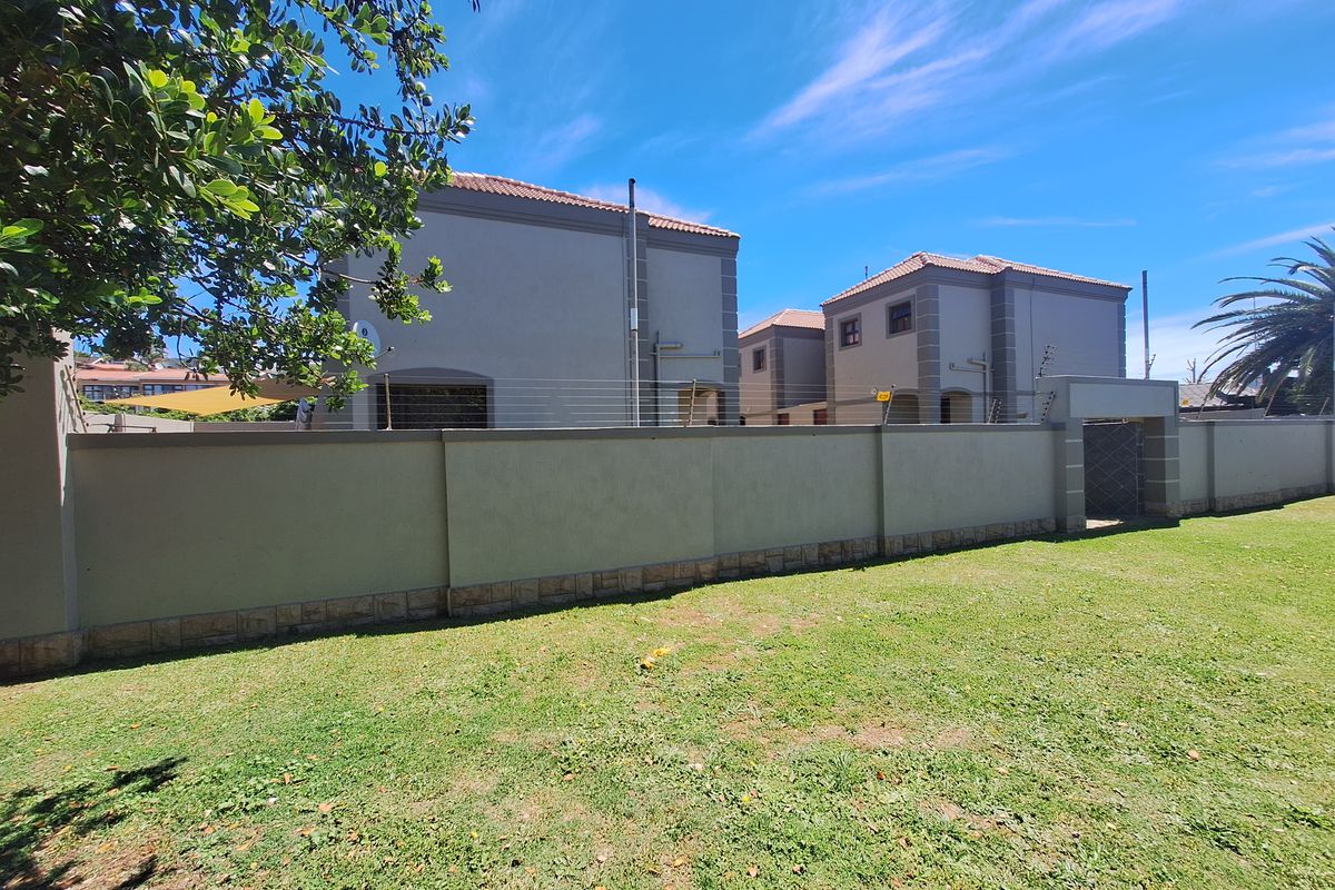 Rear view of the townhouse complex featuring a well-maintained lawn, perimeter wall with electric fencing, and stone-clad base detailing.