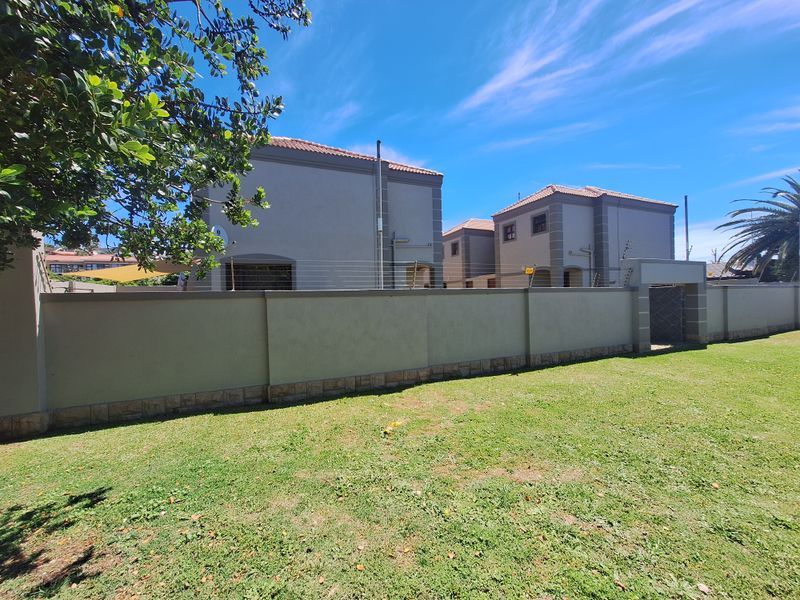 Rear view of the townhouse complex featuring a well-maintained lawn, perimeter wall with electric fencing, and stone-clad base detailing.