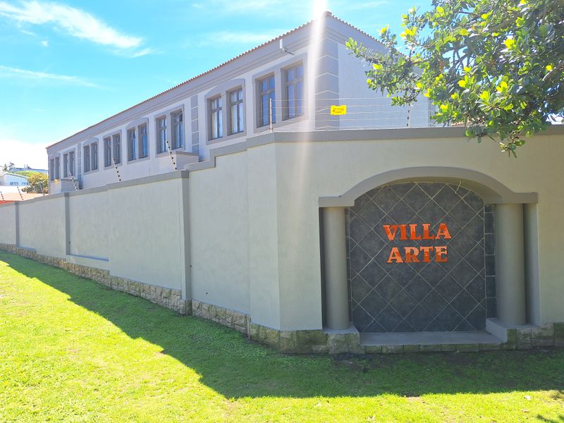 Exterior view of the Villa Arte townhouse complex featuring a secure perimeter wall with electric fencing, stone base detailing, and a modern plastered facade.