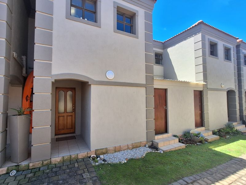 Front elevation of a modern townhouse featuring stone-clad base detailing, timber entrance doors, and paved walkways leading to the main entry.