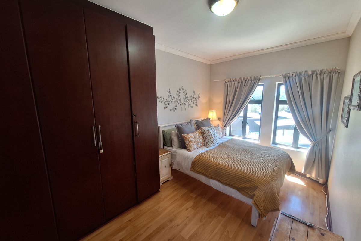 A well-maintained bedroom featuring laminate flooring, built-in cupboards, and large windows that provide natural light.