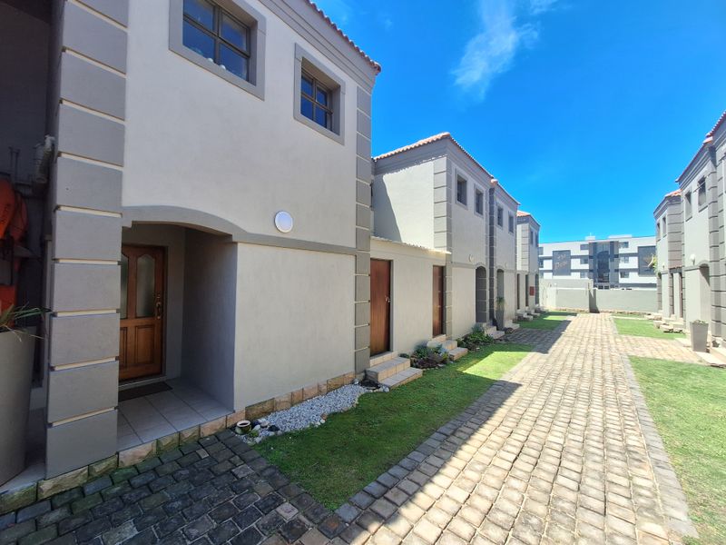 A view of the townhouse complex exterior featuring paved walkways, landscaped garden patches, and multiple entrance doors with tiled roofing.