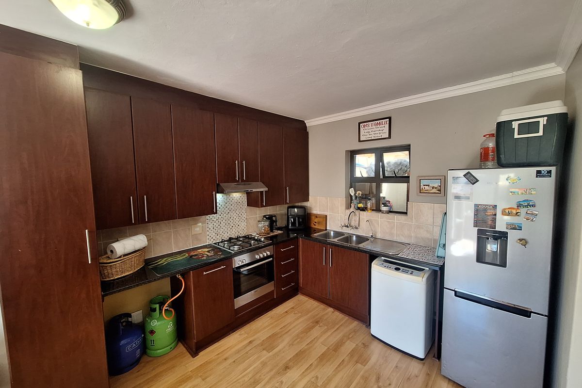 A functional kitchen featuring dark wood cabinetry, granite countertops, a gas hob, built-in oven, and a double sink with tiled backsplash.
