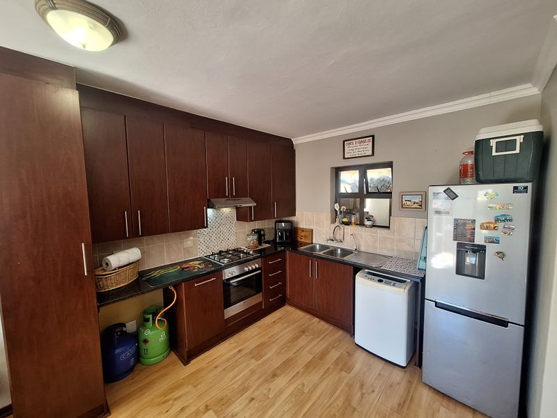 A functional kitchen featuring dark wood cabinetry, granite countertops, a gas hob, built-in oven, and a double sink with tiled backsplash.