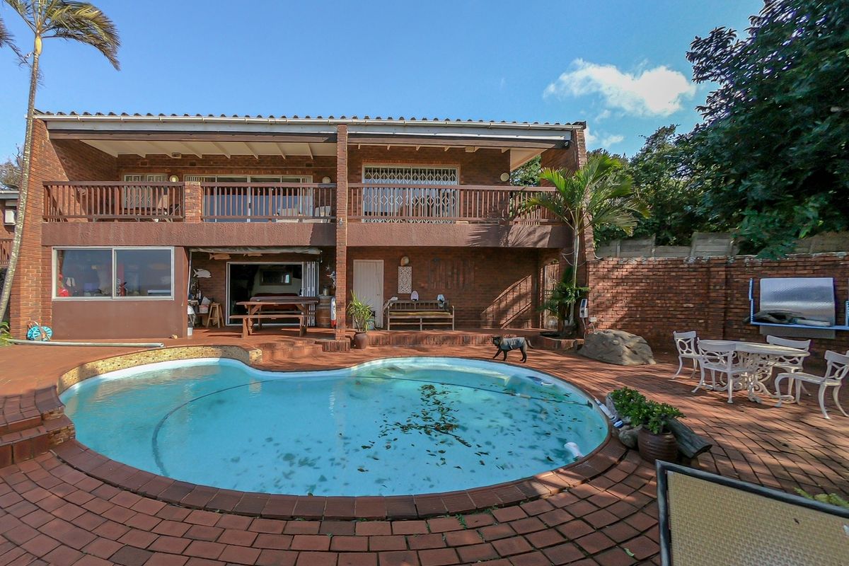 Rear exterior view featuring a swimming pool, brick paved patio area, and an upper-level balcony overlooking the garden space.