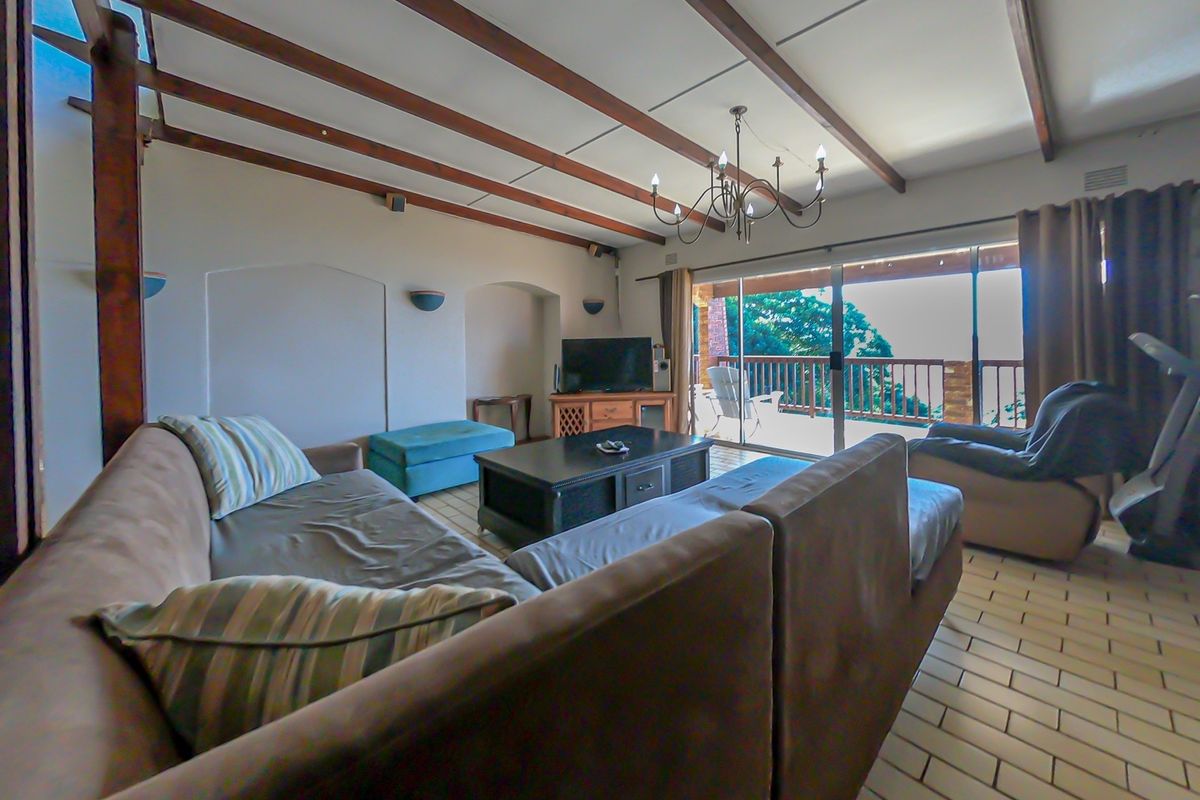 Spacious living room featuring exposed timber ceiling beams, tiled flooring, and large sliding glass doors that open onto an outdoor balcony area.